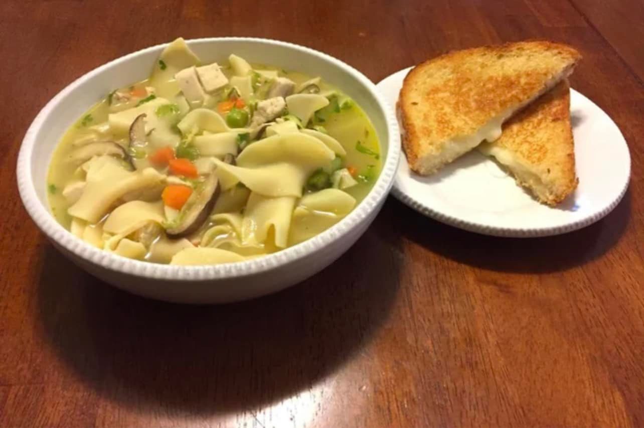 A bowl of chicken noodle soup with a grilled cheese sandwich