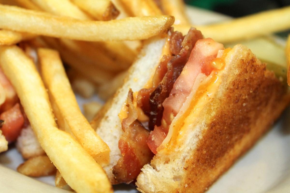 A grilled cheese with bacon and tomato and a side of fries