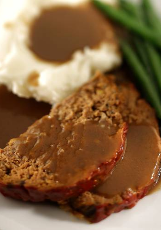 Meatloaf with gravy and green beans on a plate.